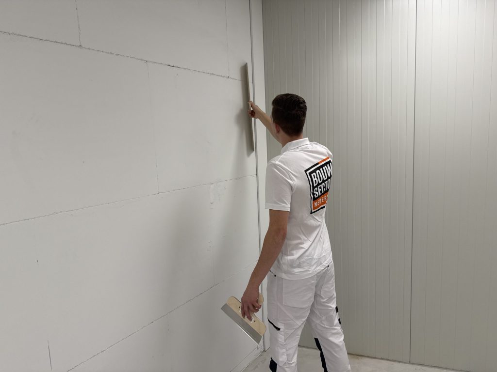 Stukadoor in wit werkpak trekt met een spaan een lange wand van gipsblokken strak