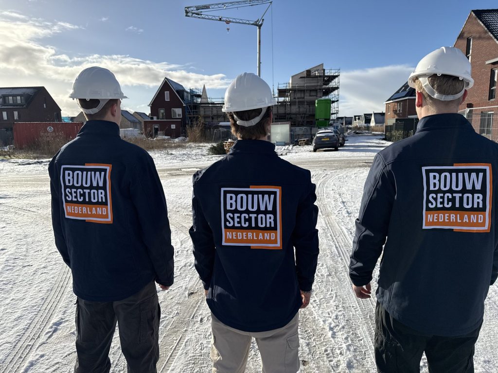 Drie vakmensen van Bouwsector Nederland met witte bouwhelm kijken naar woningen in aanbouw met steigers