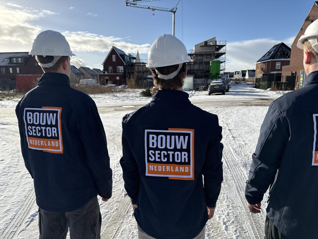 Drie vakmensen in werkkleding met het logo van Bouwsector Nederland voor een rij huizen in aanbouw
