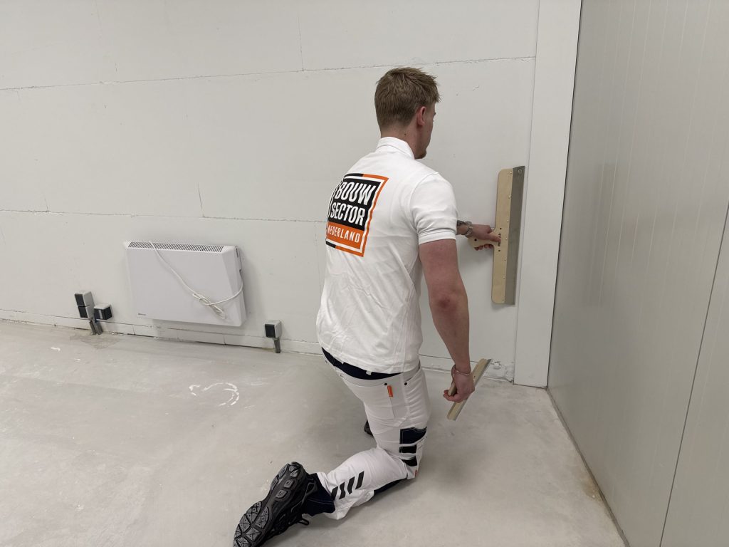 Geknielde stukadoor werkt de onderkant van een wand bij met een brede spaan